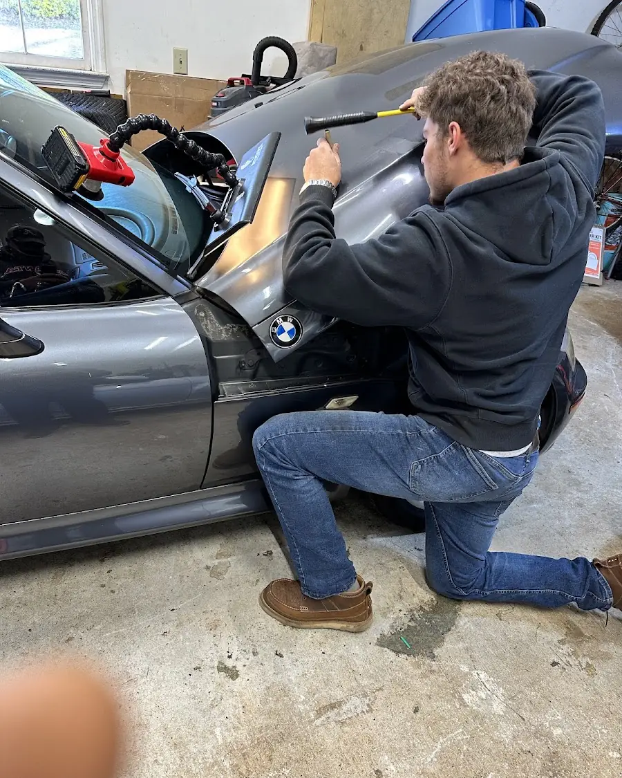 Camren working a dent out of a BMW's quarter panel from behind the trim, in the Woodstock shop