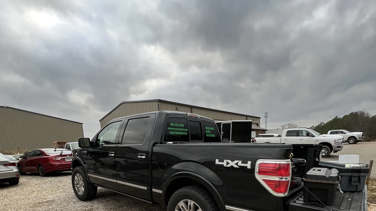 A black Ford F-150 in the shop lot under a dark storm sky