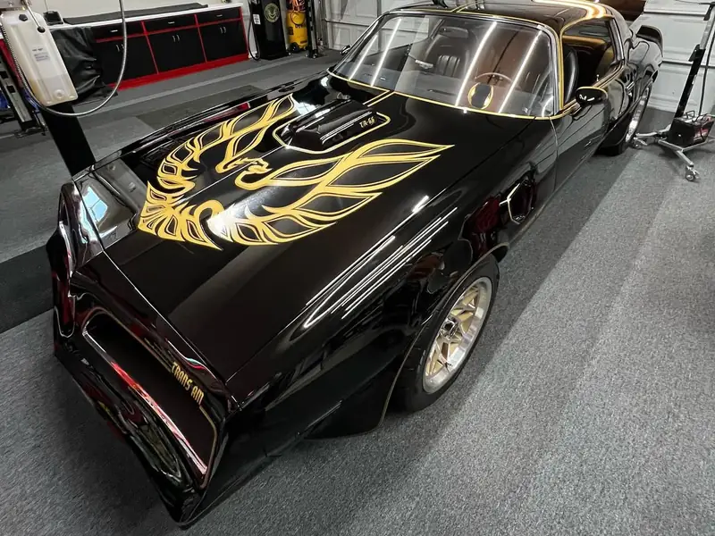 A black Trans Am with a gold hood decal, polished, on the lift