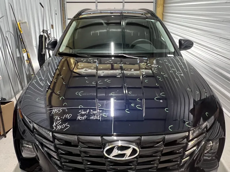 A black Hyundai in the shop with hail dents marked across the hood