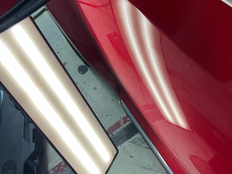 A red door panel under the dent light, the crease showing in the reflection