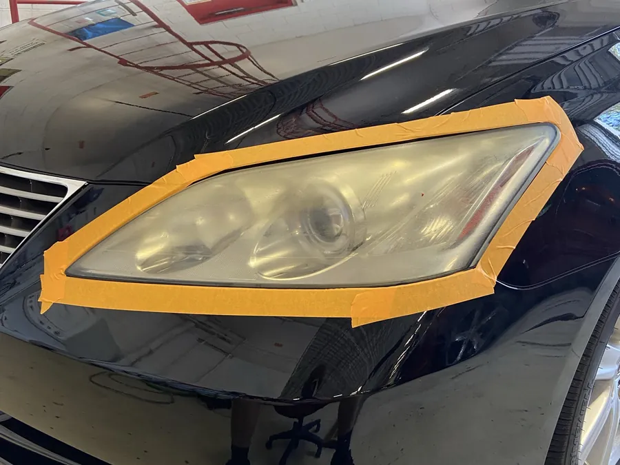 A black car with the headlight masked in tape before paint